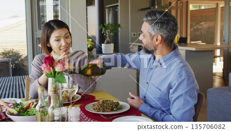 Sharing dinner Asian woman and mature man dining at home, with white wine bottle and pasta Sharing dinner Asian woman and mature man dining at home, with white wine bottle and pasta 135706082