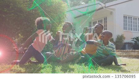 Family of four playing with bubbles on front yard lawn, with father using bubble wand 135706095