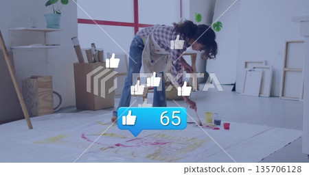 Bending artist painting on canvas in studio, with floating thumbs-up icons and like-counter graphic Bending artist painting on canvas in studio, with floating thumbs-up icons and like-counter graphic 135706128