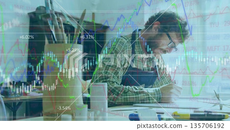 Artisan wearing apron sketching designs in workshop, with wooden model and stock market graphs 135706192