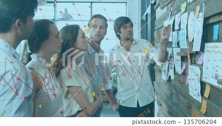 Pointing colleague showing data charts and notes on wooden wall, with digital overlay in office Pointing colleague showing data charts and notes on wooden wall, with digital overlay in office 135706204