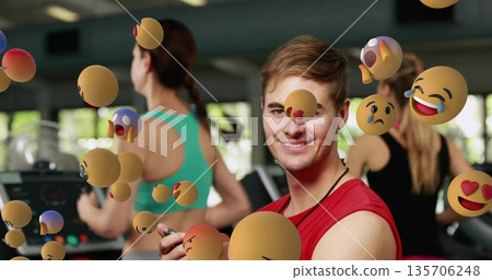 Trainer in red shirt timing runners on treadmills in gym with stopwatch, floating 3D emoji spheres 135706248