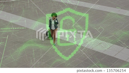 Walking executive talking on phone pulling wheeled suitcase across plaza with green lock shield Walking executive talking on phone pulling wheeled suitcase across plaza with green lock shield 135706254