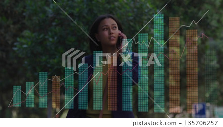 Holding smartphone to ear executive in navy blazer examining digital chart overlays on park walkway Holding smartphone to ear executive in navy blazer examining digital chart overlays on park walkway 135706257