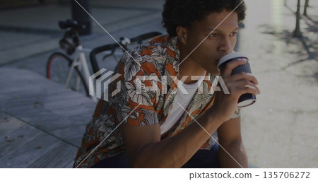 Sitting man sipping coffee on sidewalk bench by bike rack, with bicycle and cup with lid Sitting man sipping coffee on sidewalk bench by bike rack, with bicycle and cup with lid 135706272