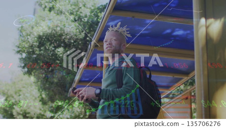 Holding smartphone, male commuter viewing financial charts at bus stop with backpack and wristwatch 135706276