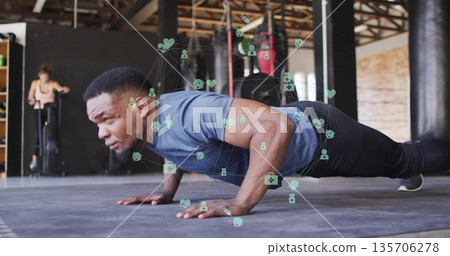Man in blue athletic shirt black pants performing push-ups at gym, with floating health icons 135706278