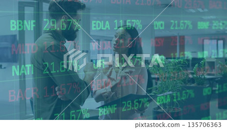 Discussing market trends colleagues in business attire holding tablet in office with stock overlays 135706363