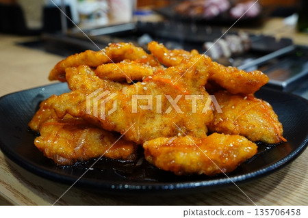 Close-Up of Crispy Sweet and Sour Pork (Guo Bao Rou) Topped with Sesame Seeds on a Black Plate 135706458