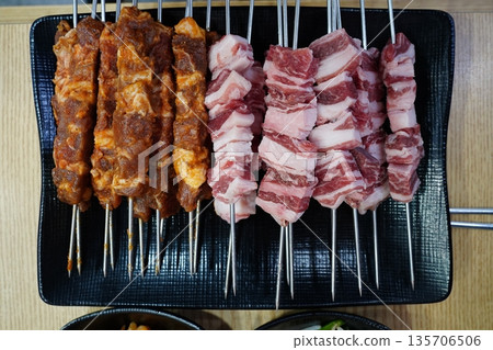 Raw and Marinated Lamb Skewers Prepared on a Black Plate 135706506