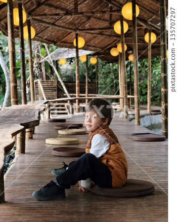 Innocent Child Sitting On Bamboo Deck With Calm Expression And Style 135707297
