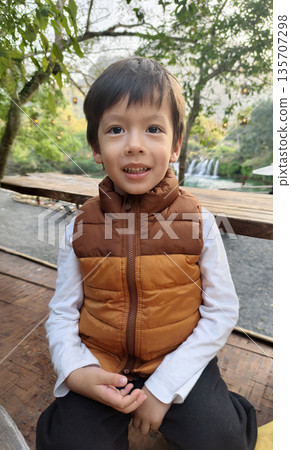 Child Posing Confidently On Wooden Railing With Scenic Waterfall Views Child Posing Confidently On Wooden Railing With Scenic Waterfall Views 135707298
