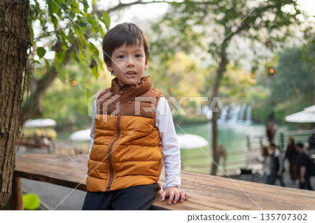 Child Posing Confidently On Wooden Railing With Scenic Waterfall Views 135707302