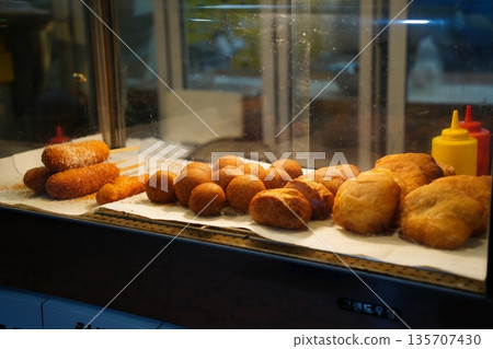 Assorted Korean Street Food Snacks, Including Corn Dogs, and Doughnuts, on Display in a Market Stall Assorted Korean Street Food Snacks, Including Corn Dogs, and Doughnuts, on Display in a Market Stall 135707430