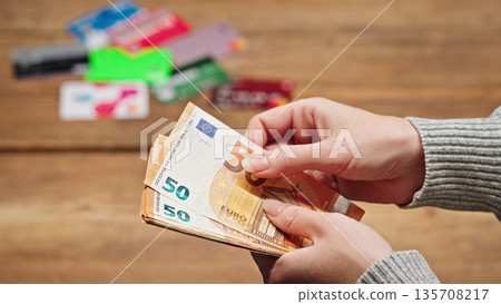 Woman counting euro banknotes with various credit cards in the background on a table, illustrating finance, payment, personal savings, and money management concepts. Woman counting euro banknotes with various credit cards in the background on a table, illustrating finance, payment, personal savings, and money management concepts. 135708217