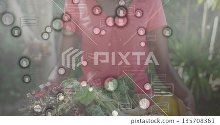 Displaying woman wearing coral T-shirt holding basket of vegetables in garden, with chat bubbles Displaying woman wearing coral T-shirt holding basket of vegetables in garden, with chat bubbles 135708361