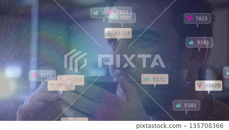 Holding smartphone, man in dark shirt viewing screen in dim interior with floating engagement icons Holding smartphone, man in dark shirt viewing screen in dim interior with floating engagement icons 135708366