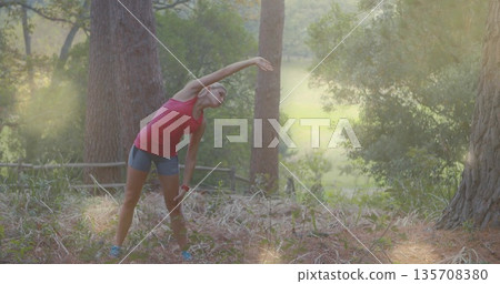 Stretching woman in sportswear doing side bend in forest clearing, with tracker, shoes, copy space 135708380
