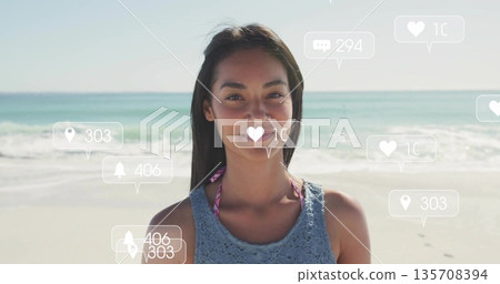 Standing woman wearing blue crochet top over pink bikini on beach, with floating social media icons 135708394