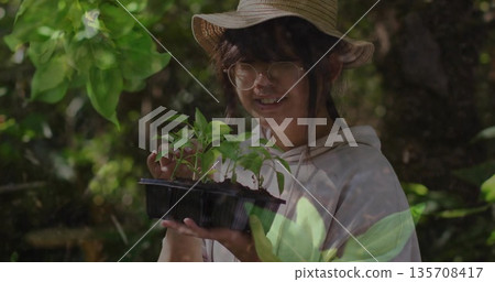 Lifting black plastic seedling tray, girl wearing straw hat and glasses touching plants in woodland Lifting black plastic seedling tray, girl wearing straw hat and glasses touching plants in woodland 135708417