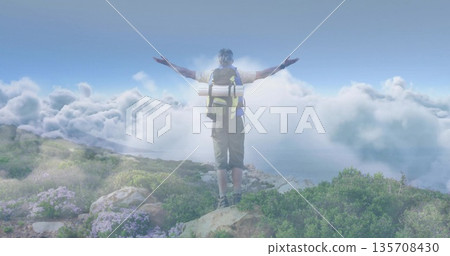 Standing hiker in shorts and boots extending arms toward clouds on mountain ridge with backpack mat 135708430