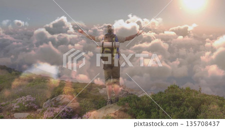 Standing hiker raising arms on rocky ridge above clouds at sunrise, showing backpack gear and boots Standing hiker raising arms on rocky ridge above clouds at sunrise, showing backpack gear and boots 135708437