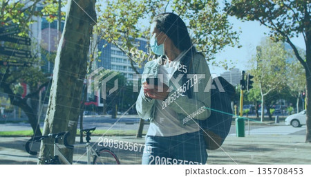 Woman wearing medical face mask holding smartphone on sidewalk, backpack and bicycle, copy space 135708453