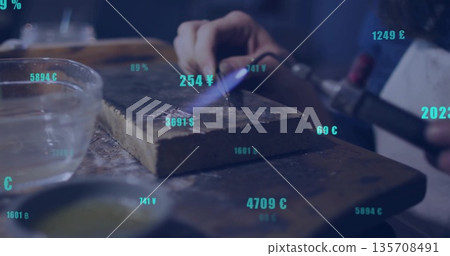 Heating metal with torch on firebrick at workbench wearing protective apron with currency symbols 135708491