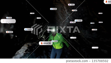 Man crouching in rocky cave tunnel with green jacket and headlamp, projecting notification graphics 135708502