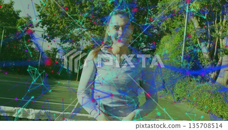 Smiling woman wearing lavender top holding racket on sunlit court, with net, fence, digital overlay Smiling woman wearing lavender top holding racket on sunlit court, with net, fence, digital overlay 135708514