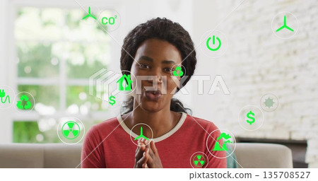 Presenting Black woman emphasizing sustainability on couch in living room, with green overlay icons Presenting Black woman emphasizing sustainability on couch in living room, with green overlay icons 135708527