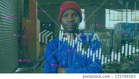 Standing technician wearing red cap and blue coverall in workshop, with financial data overlays 135708565