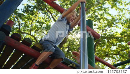Climbing child wearing striped t-shirt, shorts grabbing silver pole at park under adult hand Climbing child wearing striped t-shirt, shorts grabbing silver pole at park under adult hand 135708587