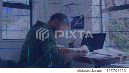 Writing man jotting notes in notebook at desk by windows, with laptop, papers and AR overlay 135708623