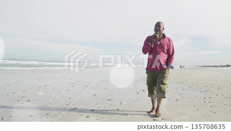 Strolling senior man barefoot wearing magenta shirt and olive shorts along sandy beach, copy space Strolling senior man barefoot wearing magenta shirt and olive shorts along sandy beach, copy space 135708635