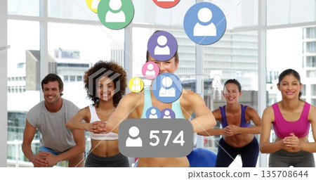 Leading female instructor guiding class through squats in fitness studio, with floating user icons 135708644