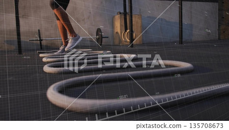 Jumping woman wearing black shorts white sneakers over battle ropes on gym floor, copy space Jumping woman wearing black shorts white sneakers over battle ropes on gym floor, copy space 135708673