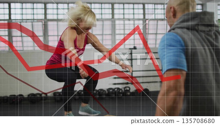 Woman doing box jump being coached by trainer in gym, kettlebells, metric overlays, copy space 135708680