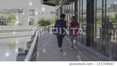 Two business casual colleagues walking waterfront walk with black shoulder bag and canal railing Two business casual colleagues walking waterfront walk with black shoulder bag and canal railing 135708687