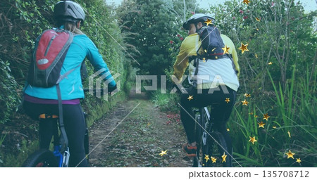 Pedaling two friends navigating through wooded trail with bikes and star-shaped light overlays 135708712