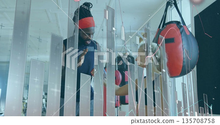 Trainee practicing boxing with coach in boxing gym, showing heavy bags, gloves, wraps, data overlay Trainee practicing boxing with coach in boxing gym, showing heavy bags, gloves, wraps, data overlay 135708758