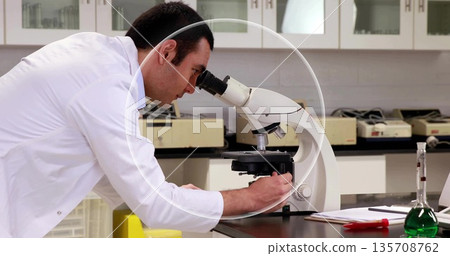 Adjusting microscope knob male scientist wearing lab coat at bench, with flask, pipette, copy space 135708762