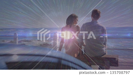 Sitting couple in dress gazing waterfront view from bench on deck at night, with lens flare Sitting couple in dress gazing waterfront view from bench on deck at night, with lens flare 135708797