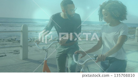 Walking couple holding bicycles on seaside promenade, with ocean waves and metal railing Walking couple holding bicycles on seaside promenade, with ocean waves and metal railing 135708810