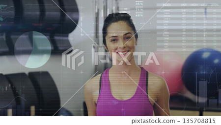 Tracking athletic woman wearing bright pink sports top lifting dumbbell in gym, with data overlay Tracking athletic woman wearing bright pink sports top lifting dumbbell in gym, with data overlay 135708815