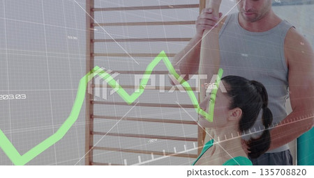 Fitness instructor supporting client stretching against wooden stall bars in gym, with green graph Fitness instructor supporting client stretching against wooden stall bars in gym, with green graph 135708820