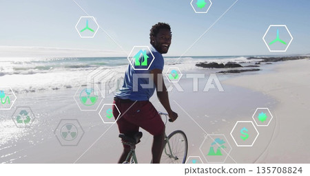 Smiling African American male pedaling bicycle along sandy shoreline, with hexagonal eco icons Smiling African American male pedaling bicycle along sandy shoreline, with hexagonal eco icons 135708824