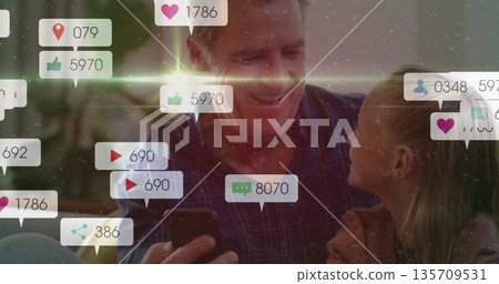 Watching grandfather and granddaughter scrolling phone in backyard patio, with social media icons 135709531