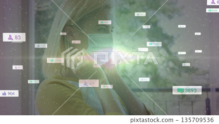 Securing surgical mask woman in yellow top by window, floating icons and lens flare, copy space Securing surgical mask woman in yellow top by window, floating icons and lens flare, copy space 135709536