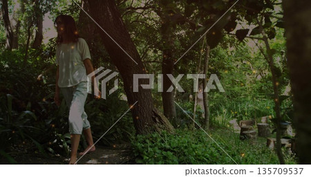Walking woman wearing white T-shirt and pants along dirt path in garden, with stumps, copy space Walking woman wearing white T-shirt and pants along dirt path in garden, with stumps, copy space 135709537